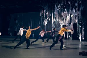 Gruppe auf der Bühne in synchroner Bewegung und glänzender Kleidung