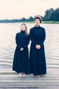 two women in black dresses, standing next to each other at a lake