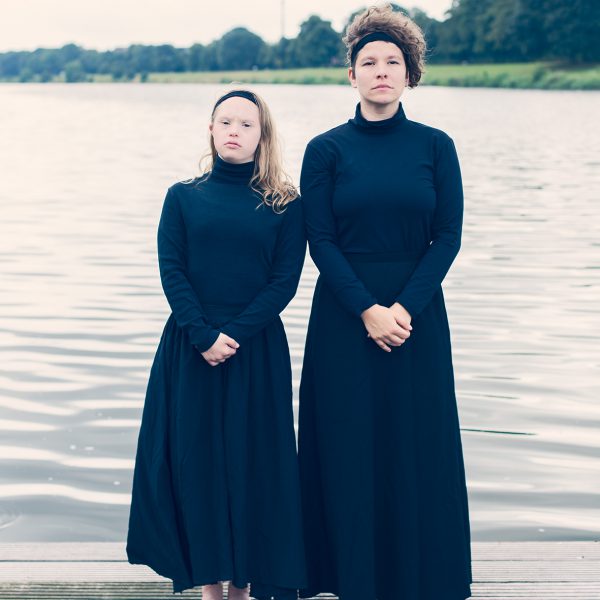 two women in black dresses, standing next to each other at a lake