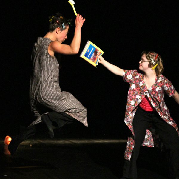 eine Tänzerin mit einer Bürste in der Hand springt vor einer anderen Tänzerin hoch