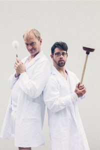 two performers pose with a toilet brush and a plunger