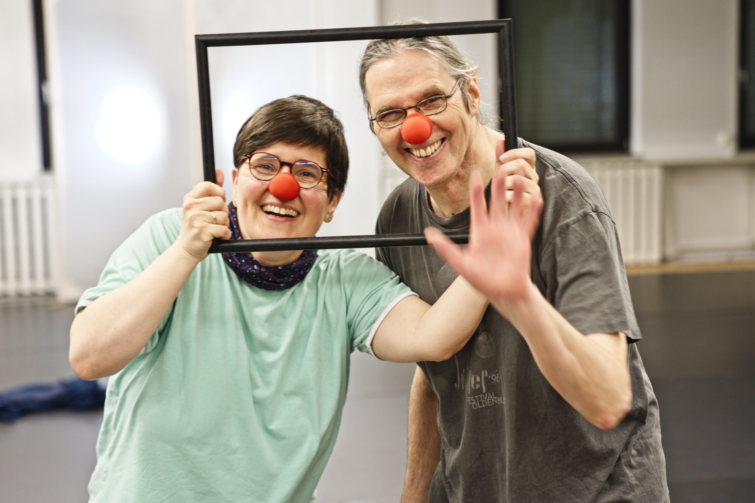 Zwei Clown:innen halten einen Bilderrahmen und schauen gemeinsam hindurch