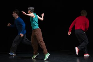 three dancers running in a black room