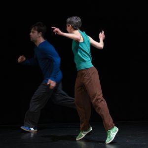 drei Tänzer:innen rennen in einem schwarzen Raum