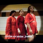 Filmbild aus Bad Luck. 3 Darsteller:innen stehen in Rot gekleidet im Profil und schauen in die Kamera