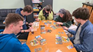 5 Menschen sitzen um einen Tisch und spielen ein Brettspiel