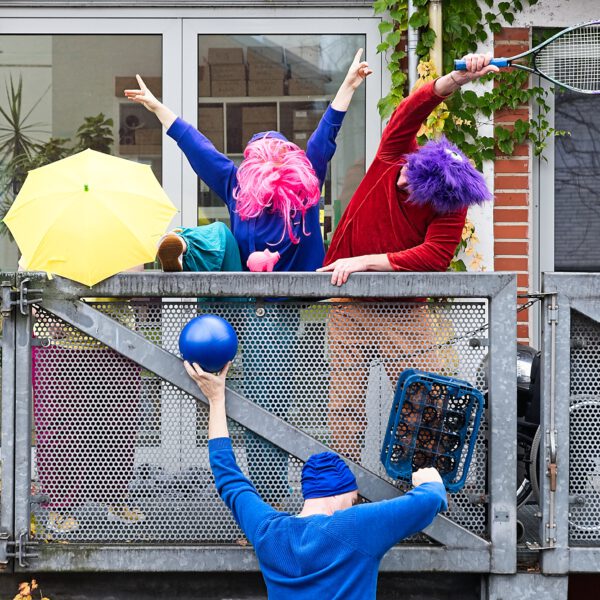 4 Personen mit Bällen, Schirmen, Kisten und bunten Perücken bilden eine Installation am Geländer.