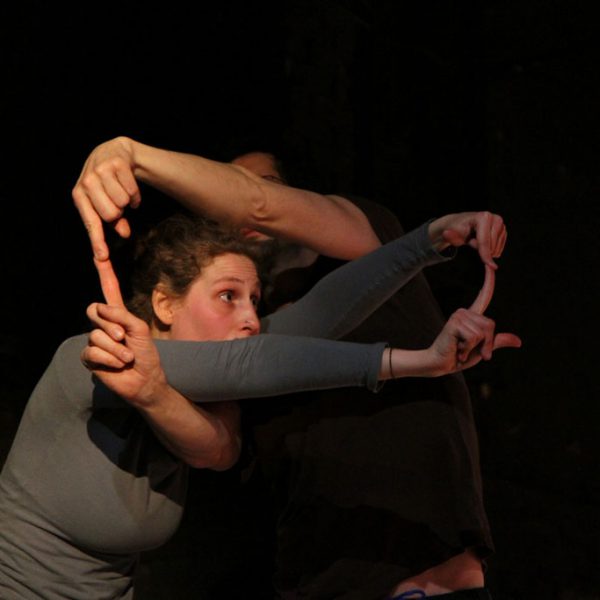 Two dancers cross their arms and touch each other' s fingers.