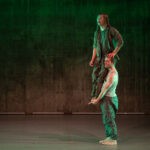 Die Bühne ist grün erleuchtet, die zwei Tänzer in Tarnkleidung bauen miteinander eine Räuberleiter. Der ober hält Ausschau